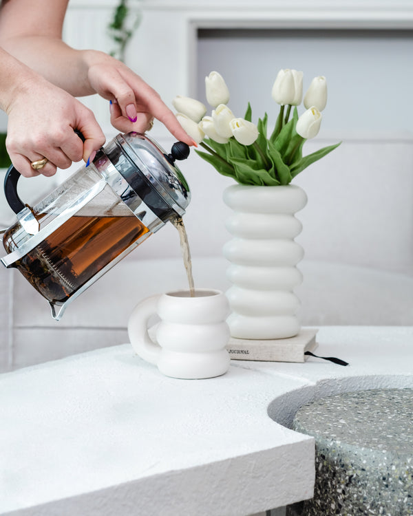 Someone pouring tea out of a Presspot into a mug, with some tulips in the background