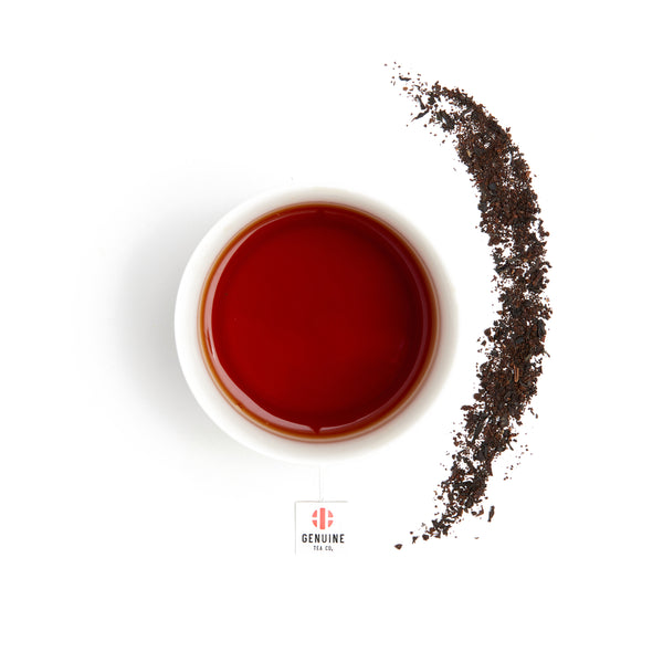 Overhead view of a brewed cup of Organic Assam Breakfast Tea, next to some tea leaves 