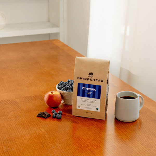 12oz bag of Ethiopia coffee on a table next to a mug, blueberries, and peaches.